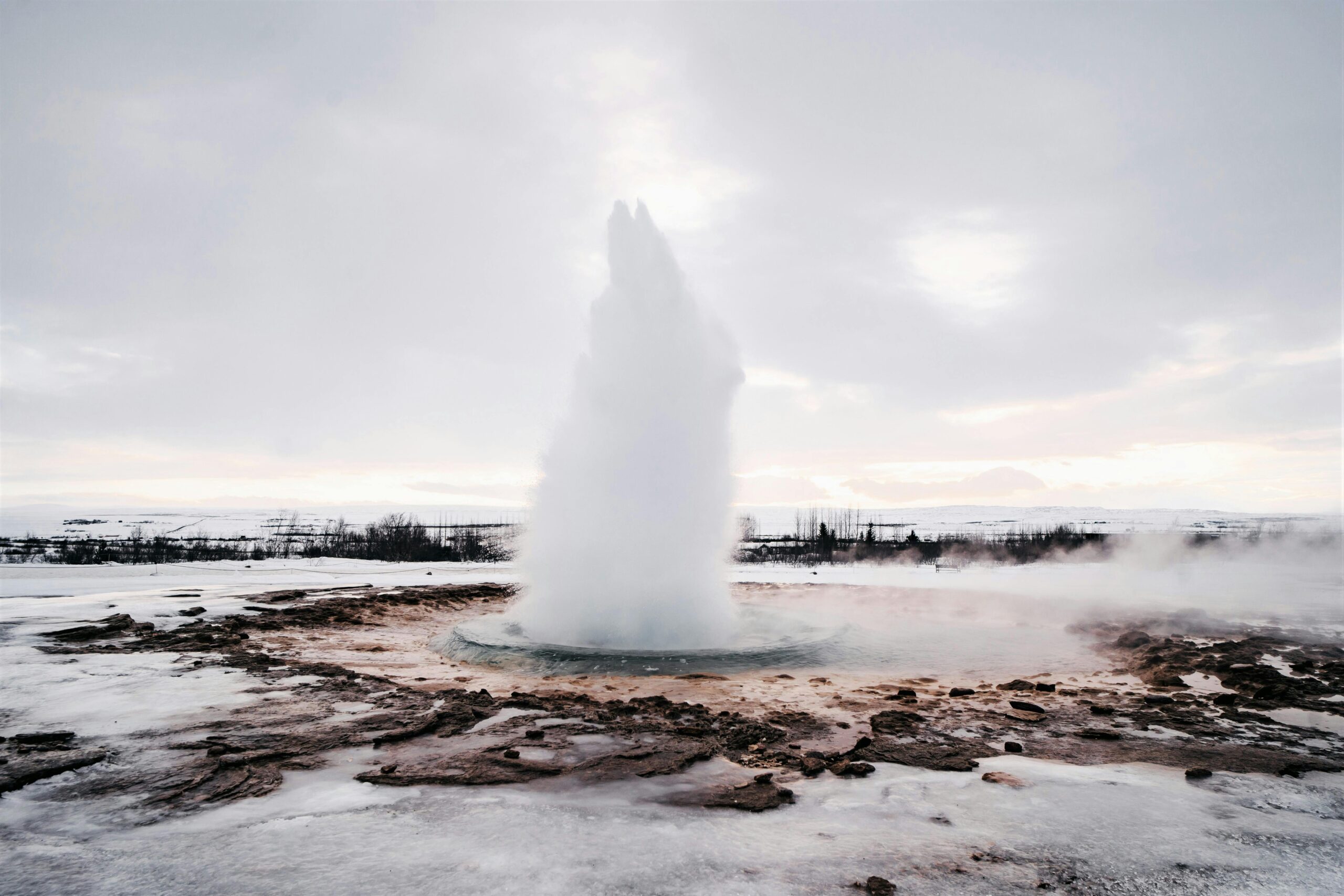 Foto van de uitbarsting van de Strokkur geiser in het zuidwesten van IJsland, waarbij water meters hoog de lucht in spuit.