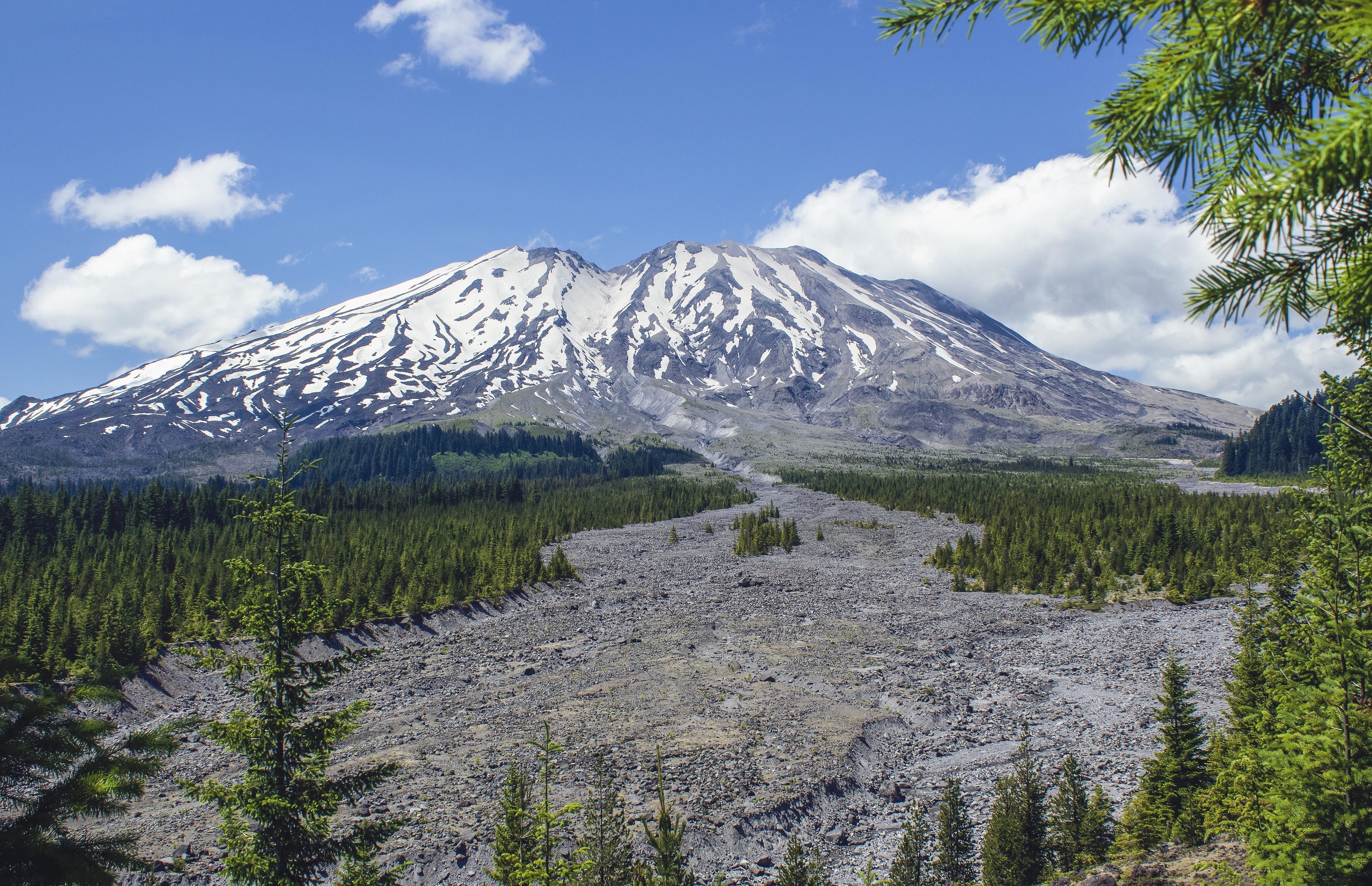 Deze foto illustreert het begrip geomorfologie: te zien is een foto met een vulkaan op achtergrond en kleine stenen op voorgrond die zijn ontstaan en getransporteerd door de geologische processen van verwering en erosie.