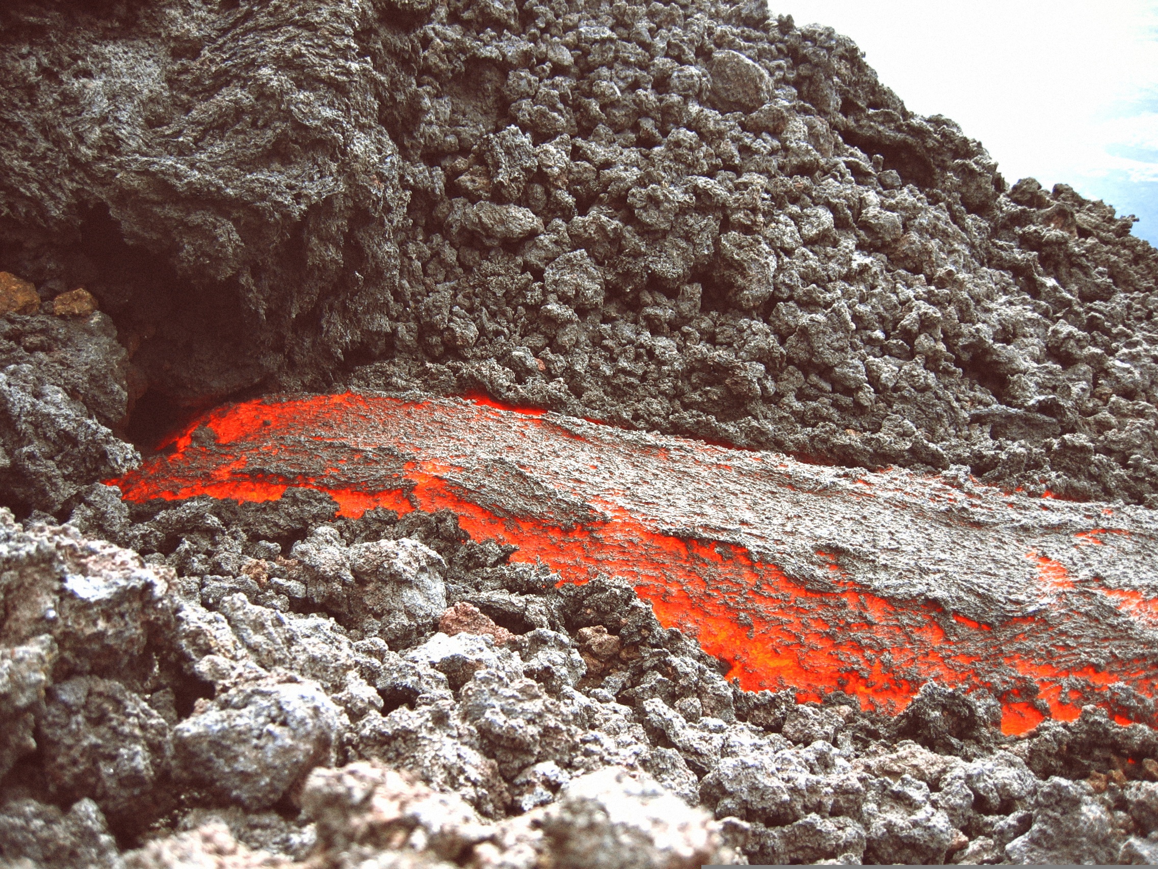 Deze foto toont verschillende vormen van vulkanisch materiaal: gloeiend hete lava, vulkanische as en vulkanisch gesteente.